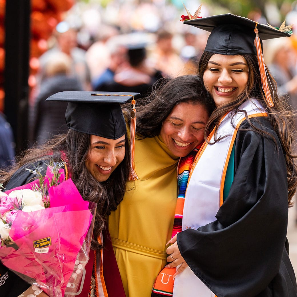 Three females, two are wearing commencement regalia