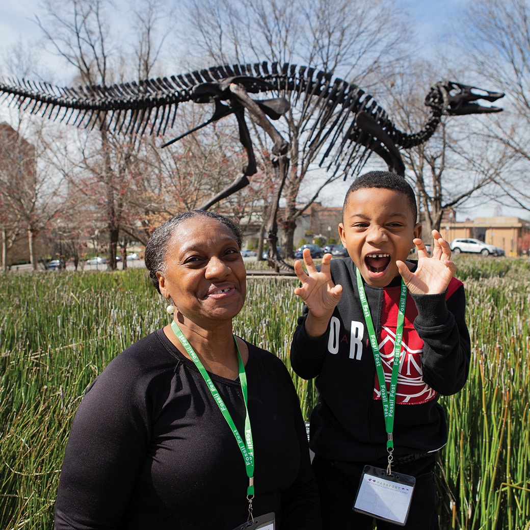 A woman and a young child stand in front of a dinosaur skeleton