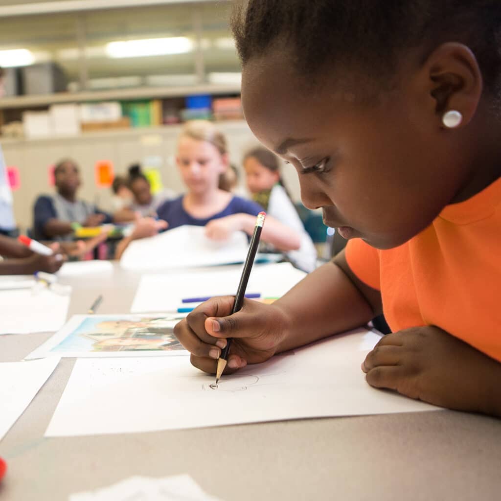 A young girl writes on a piece of paper in front of her