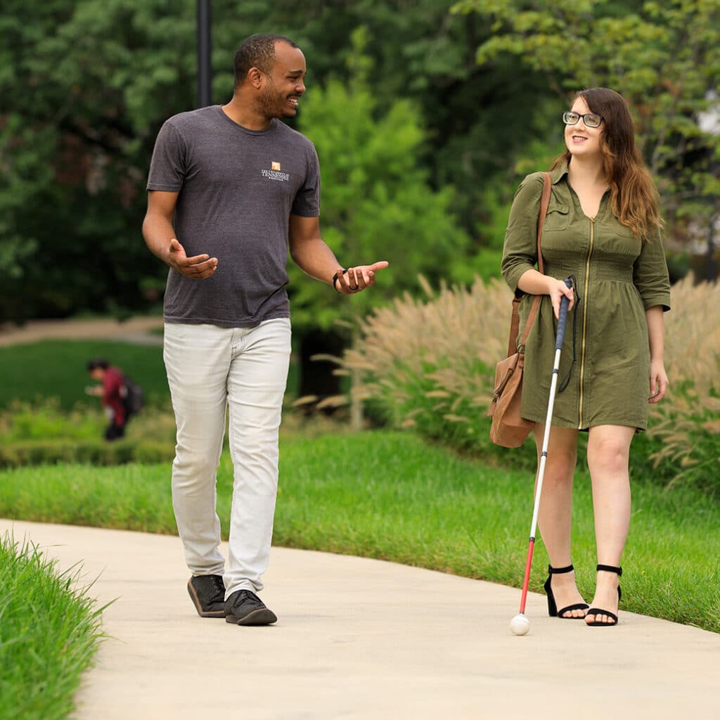 A man and a woman with a cane walk on a pathway