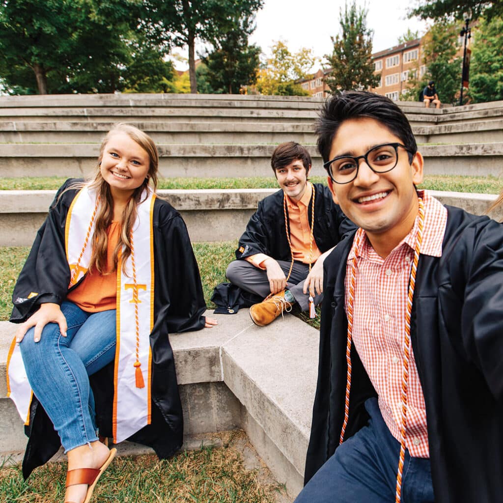 Students in commencement regalia pose for a selfie on campus