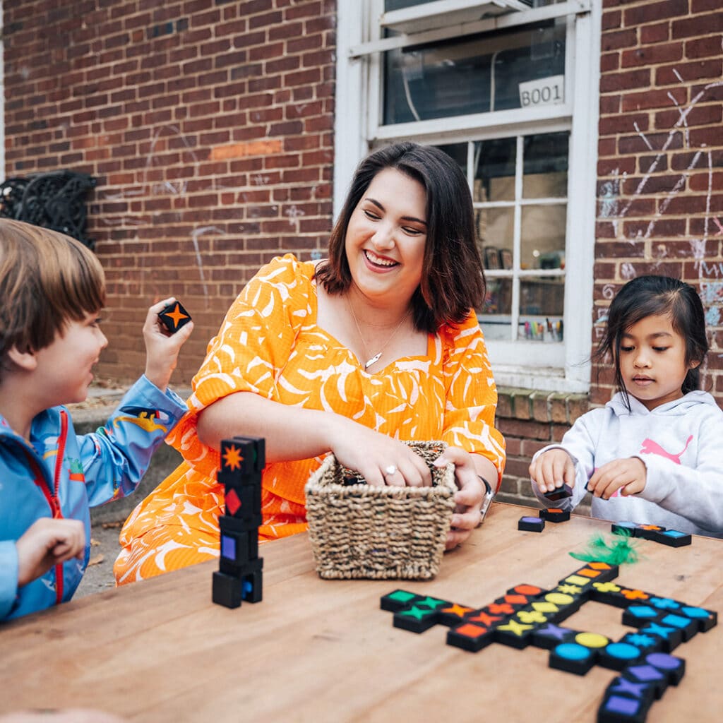 A woman in an orange dress does learning activities with young children