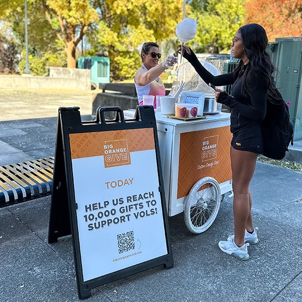 A student gets cotton candy. Next to her is a sign with an interesting fact about donor support at UT.