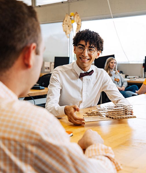 An Architecture and Design student shows a small building model to another student