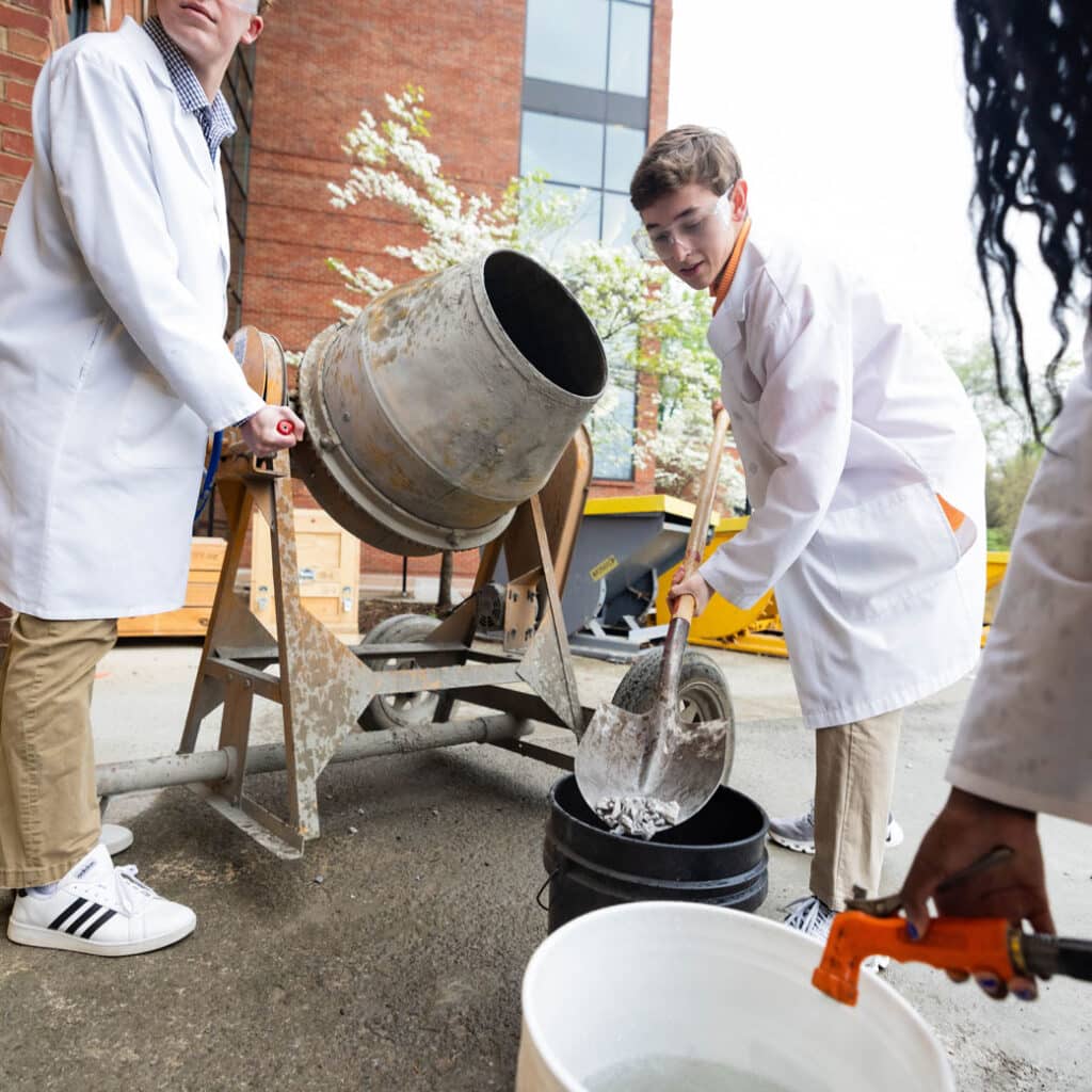 A student in a lab coat and goggles works with cement