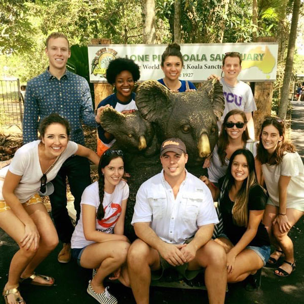 Zach Campbell and a group of people pose for a photo in front of a koala sanctuary sign