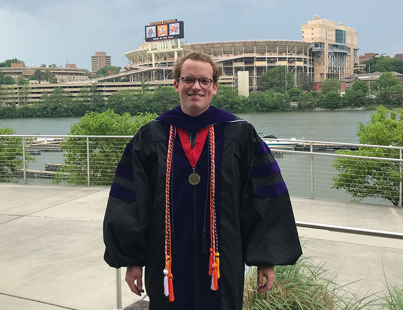 Zach Campbell in commencement regalia with Neyland Stadium in the background