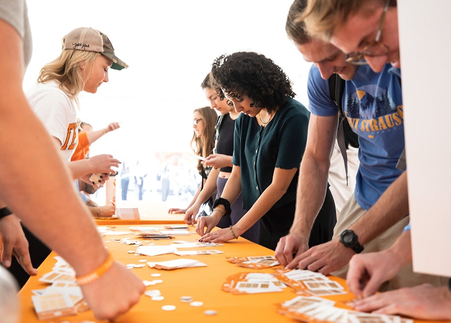 bog-matches-challenges Students stand on opposite sides of a table with an orange tablecloth and play a Big Orange Give scratch game