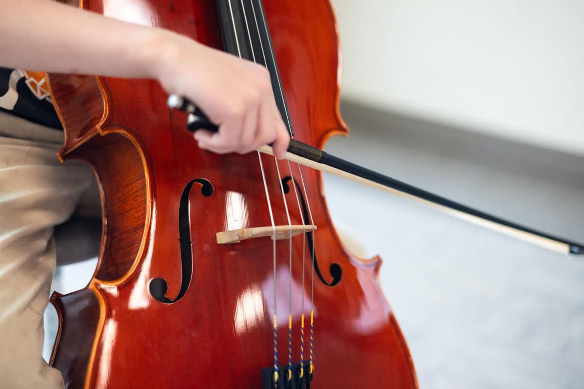 arthur-stephen-cello-1200x800 Close up of a hand playing a cello with a bow.