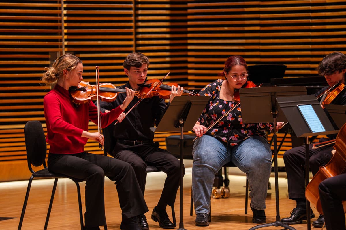 string-project-2024-26-ut-student-teachers-1200x800-1 Four UT String Project student teachers performing on stage during a recital.
