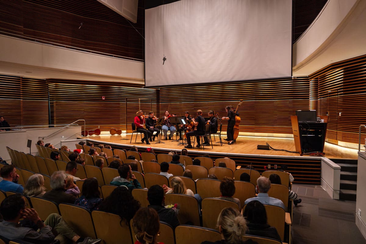 string-project-2024-26-ut-student-teachers-1200x800-3 Nine UT String Project student teachers perform on a stage in front of a crowd.