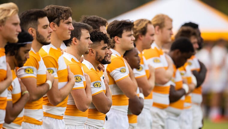 Rugby players standing in a line with their right hands over their chests.
