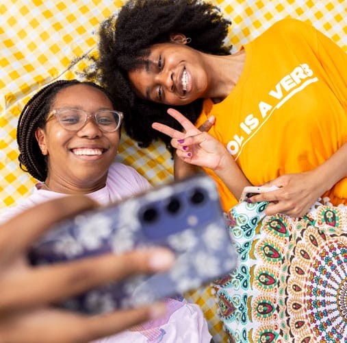 fye-2025-gallery-students Two students lying on an orange and white checkered blanket snap a selfie.
