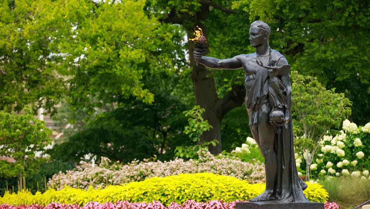 The Torchbearer Statue in front of a backdrop of spring greenery and flowers.