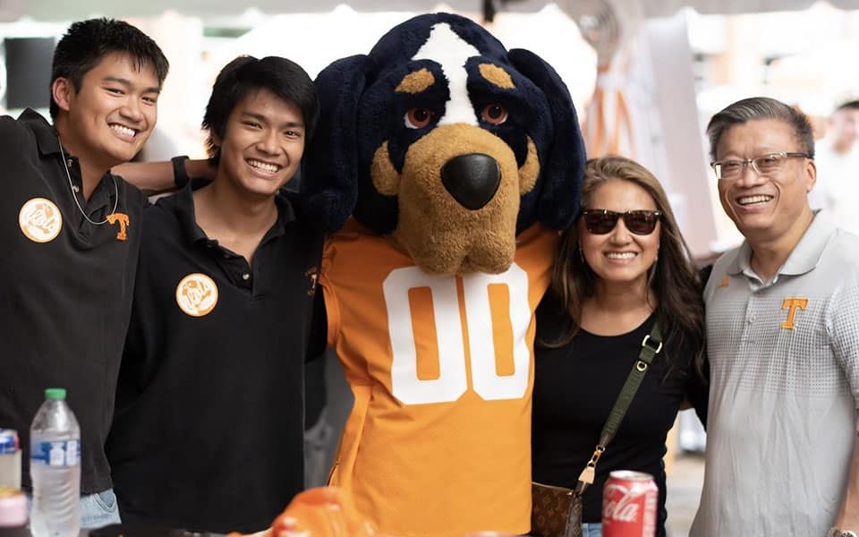 Denise Tran, Jonathan Mai, and their two sons pose for a photo with the Smokey mascot during a 2023 UT alumni tailgate.