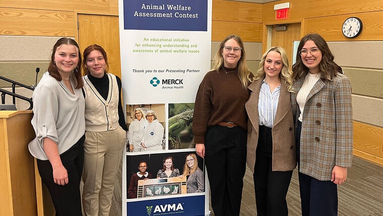 Five students stand next to an animal welfare assessment contest pop-up banner.