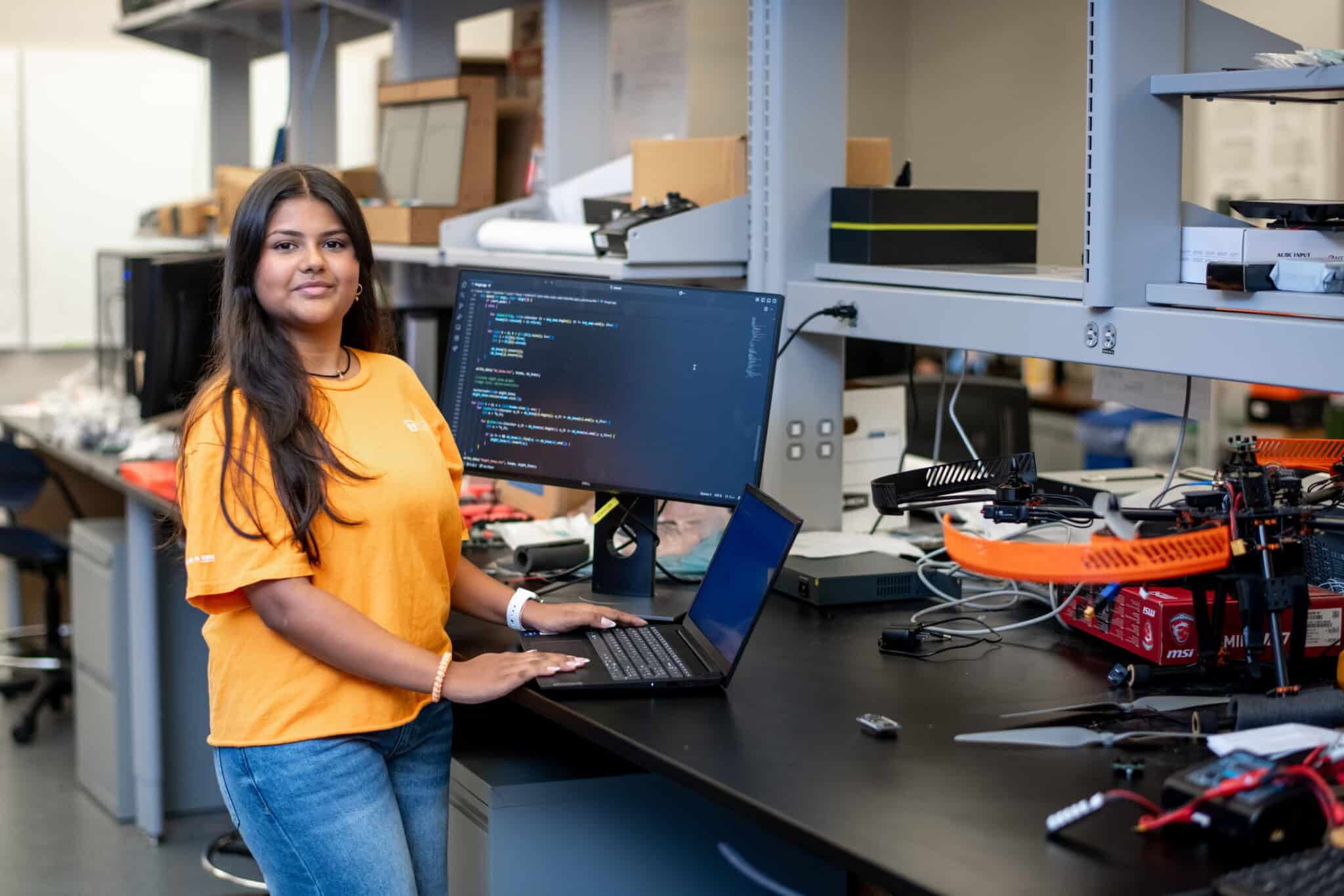 Woman in orange shirt smiling in a comuter science lab at the university of tennessee