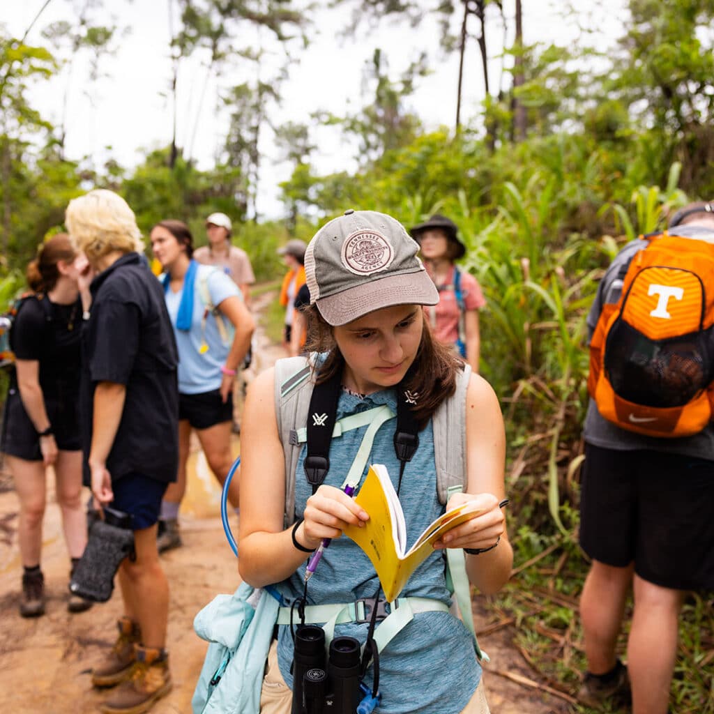 UT student in rainforest looking at a book