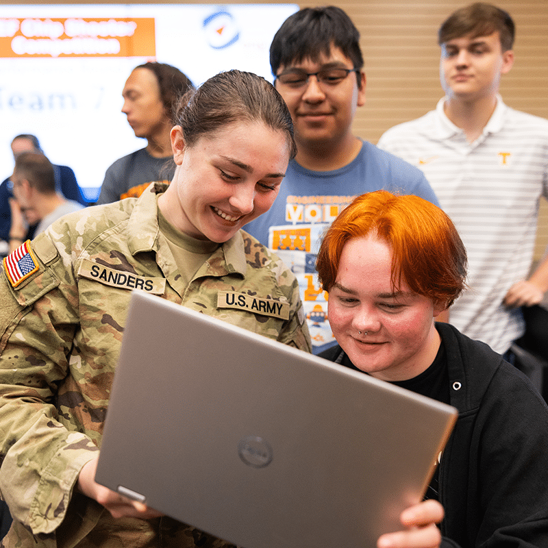 Students in military uniforms looksing at computer screen smiling