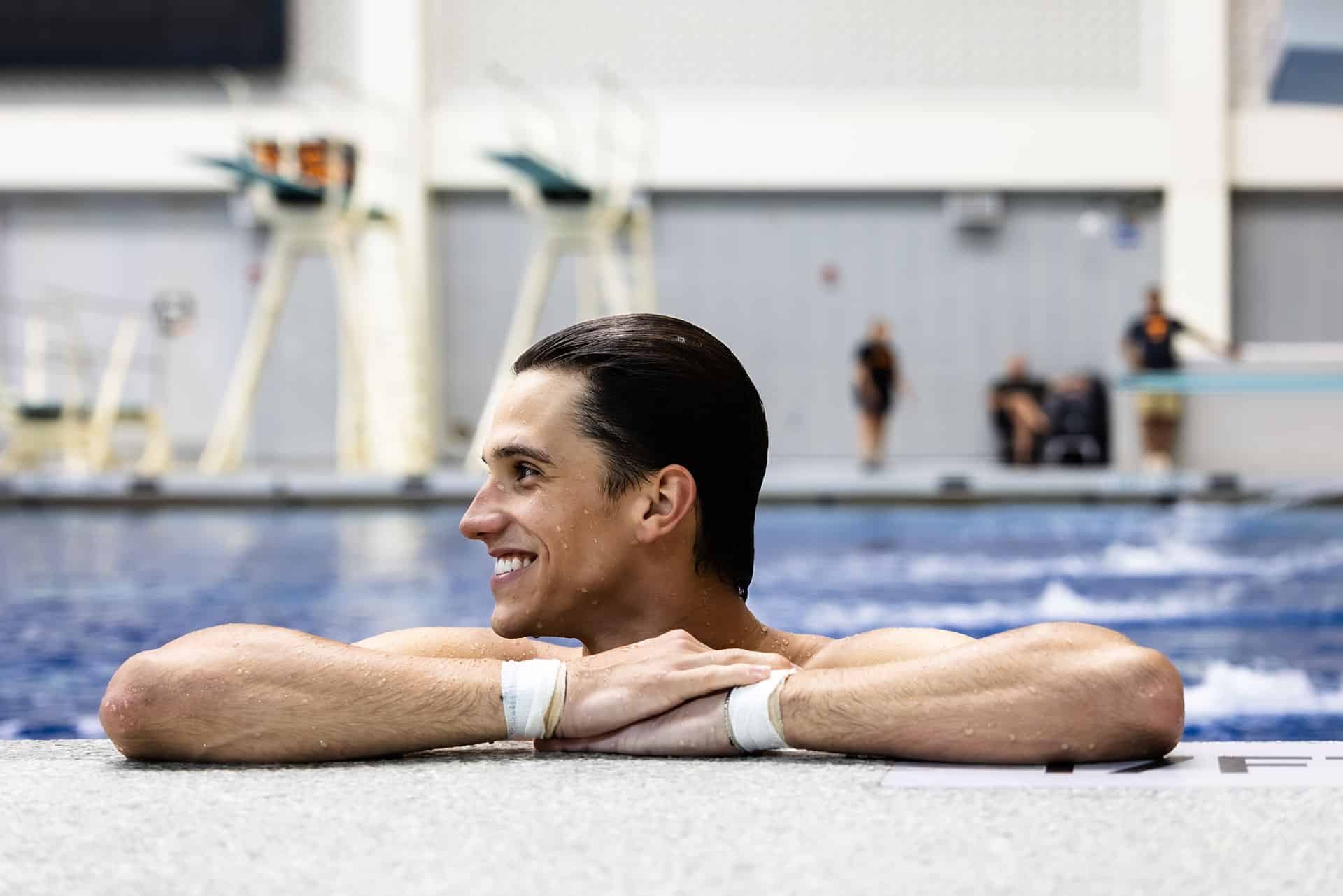 A person smiling while leaning on the ledge of a swimming pool.