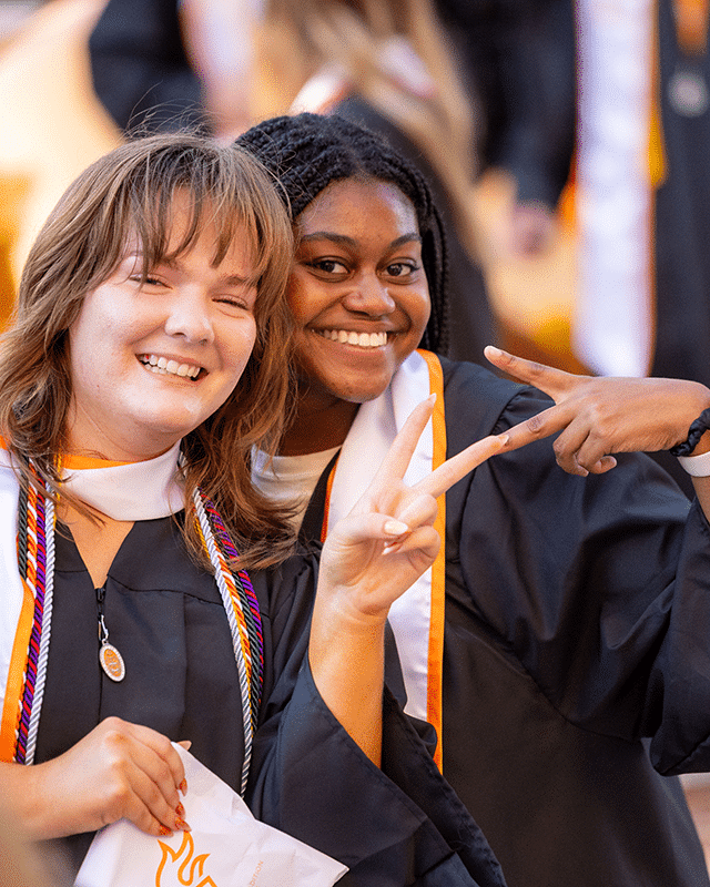 two students in graduation outfits smiling